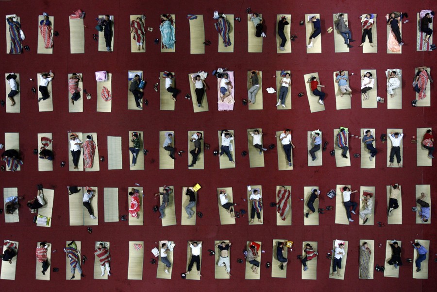 An overhead view of dozens of people lying on mats organized on the floor of a gymnasium