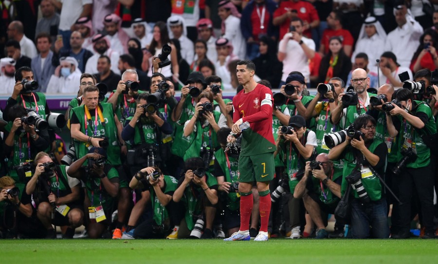 A soccer player wets his hands using a water bottle, as a couple dozen photographers standing behind him take photos.