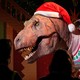 People look at a life-size T. rex sculpture dressed in a Santa hat and festive sweater.