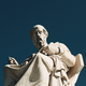 Color photograph of a marble statue of Plato seen in front of a dark-blue background.
