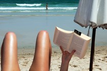 someone reads a book on the beach, their legs are visible