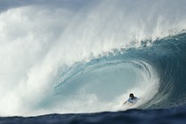 A surfer rides low inside the barrel of a huge breaking wave.