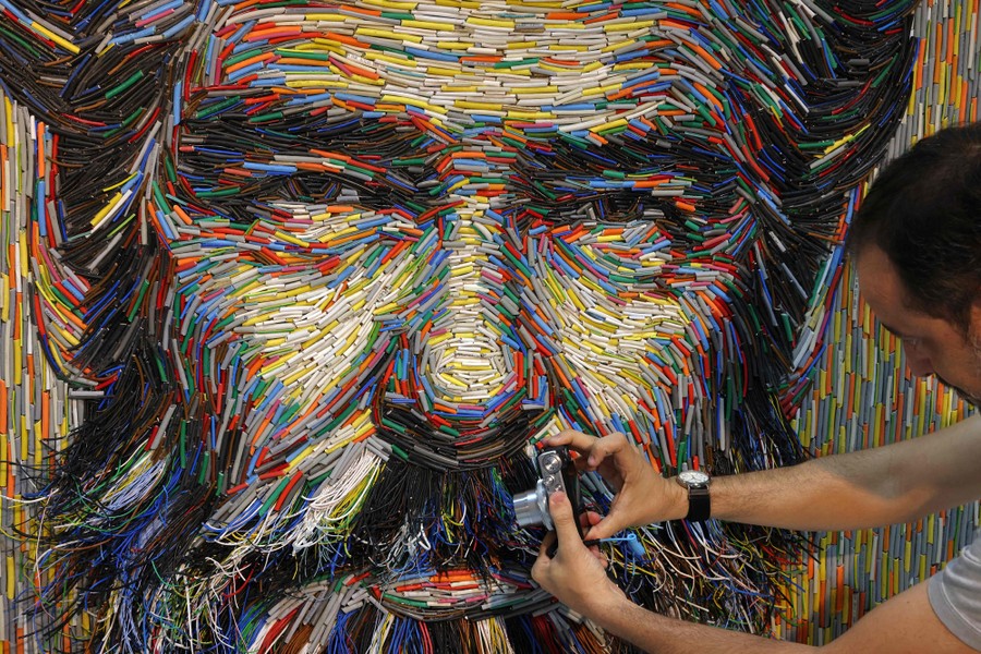 A person takes a photo of a large portrait of a bearded man, made up of pieces of insulated wire.