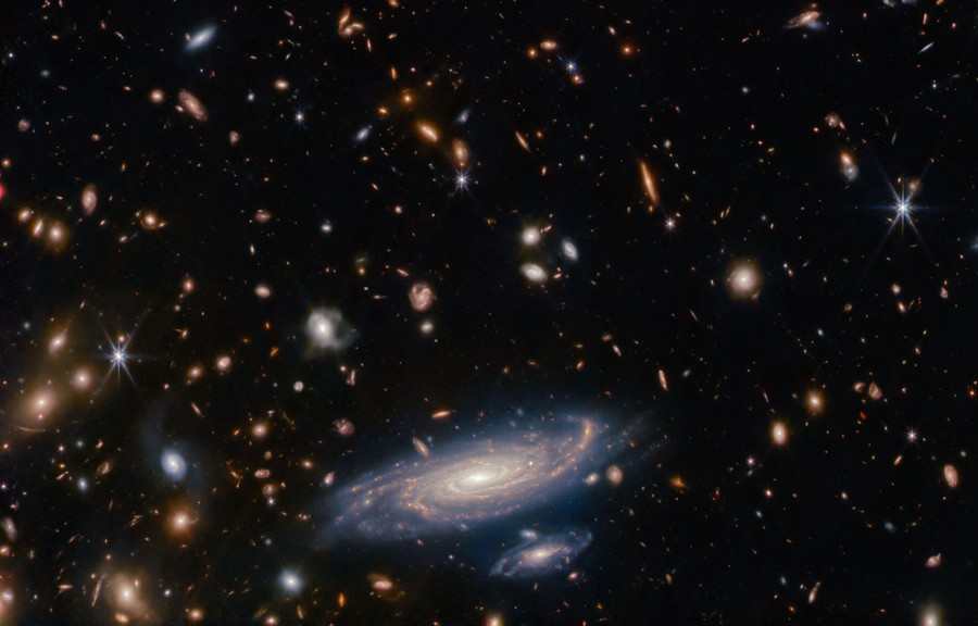 Many small, distant galaxies fill the image, with a pair of closer, larger-seeming spiral galaxies at bottom center.