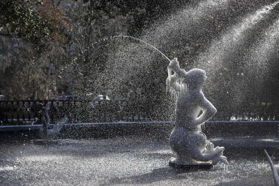 Ice clings to a cherub sculpture in a fountain on a chilly day.