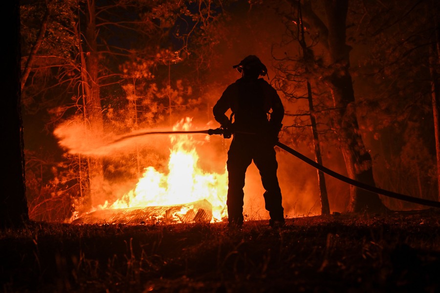A firefighter sprays water toward part of a wildfire in a forest.