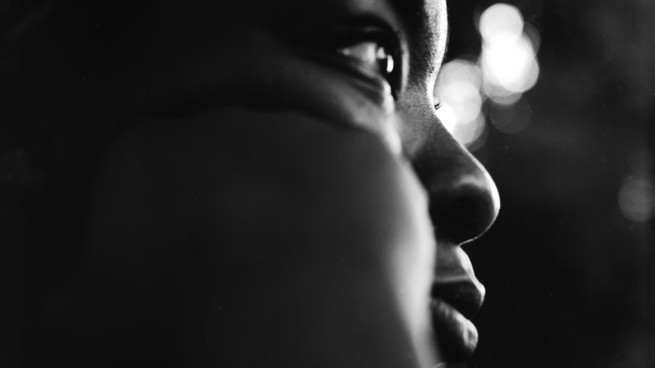 A photograph of someone's face in profile, in black and white, looking off into the distance