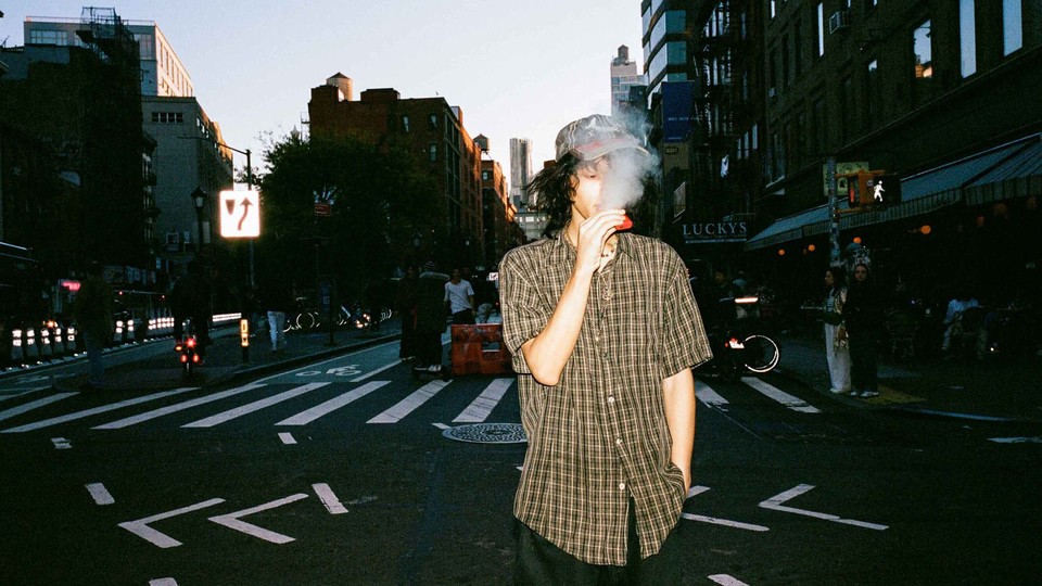 A color photograph of a man vaping on the street.