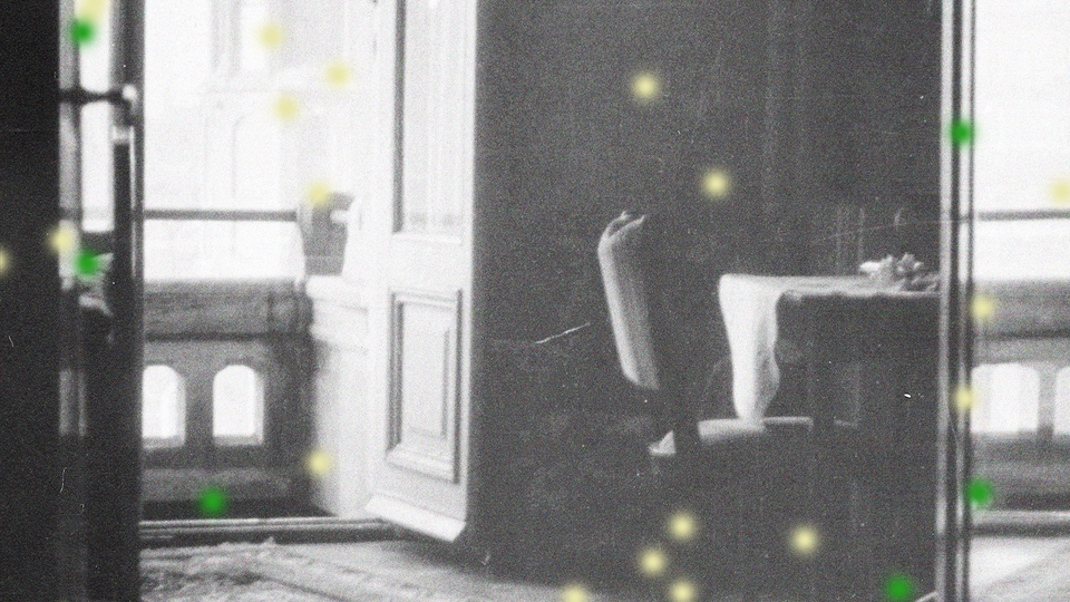 Black-and-white photo of table and chair near open balcony doorway with green and yellow dots