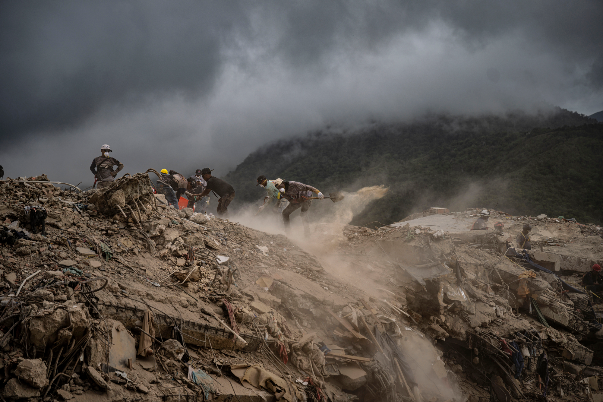 rescue workers in helmets and masks dig through a large pile of dirt and rubble 