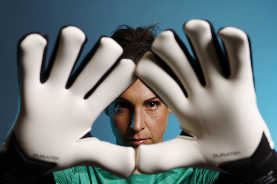 A goalkeeper poses, holding her gloved hands up in front of her face.