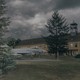 photo of fighter jet with German markings on concrete pad, behind a tree, with long building behind and stormy gray skies
