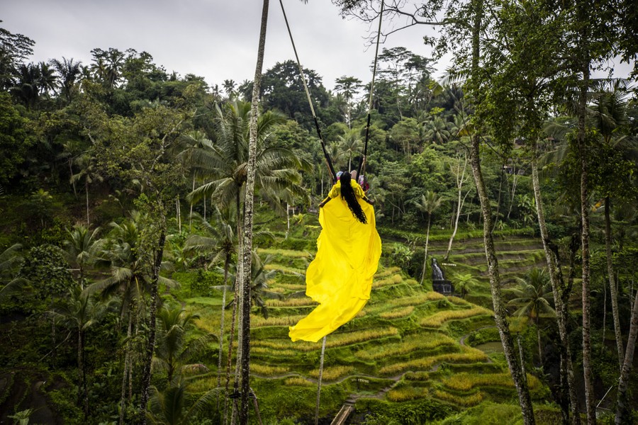 A woman in a long yellow dress swings in a forest.