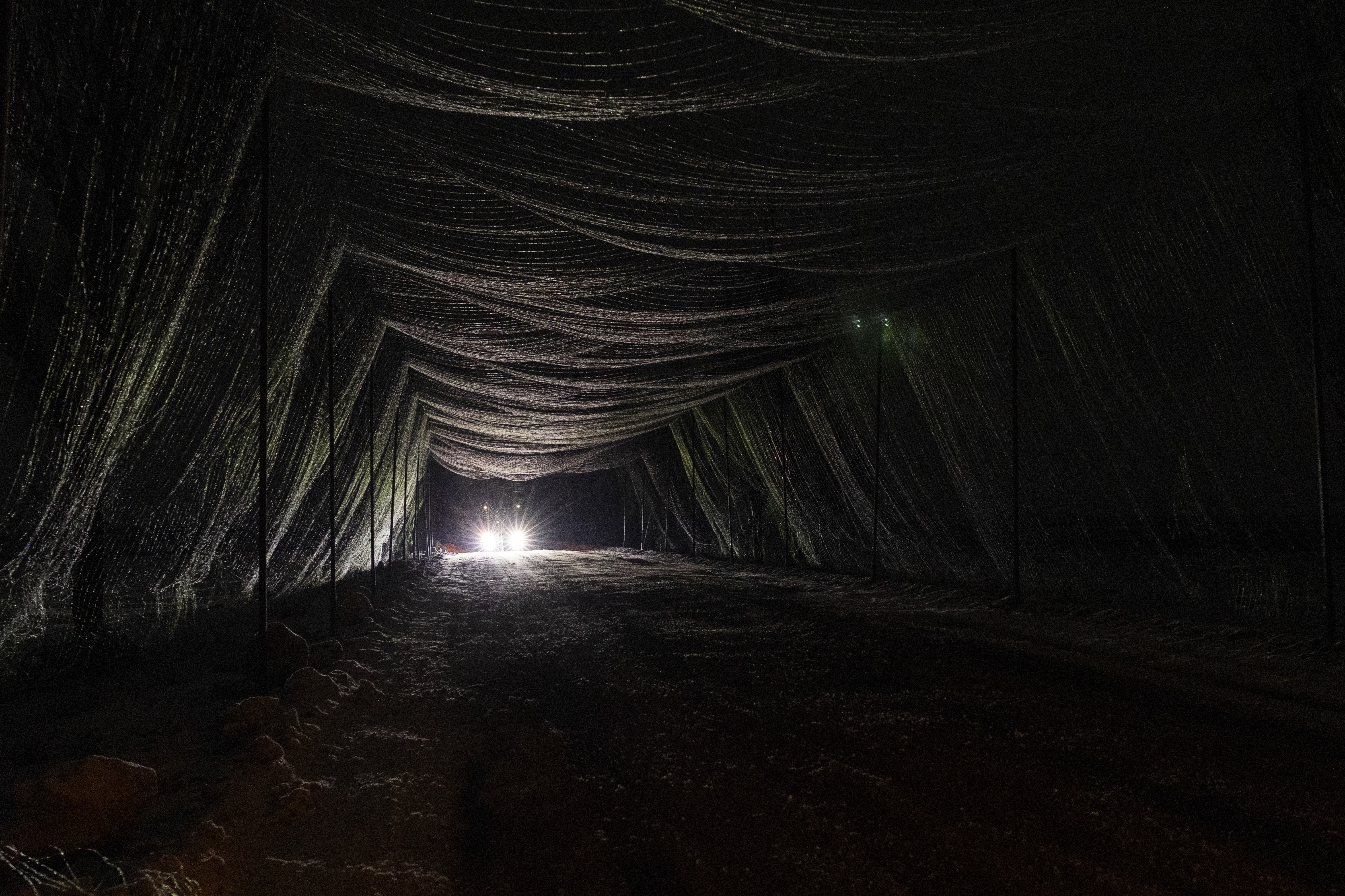 A vehicle travels at night along road section that has been covered with anti-drone netting.