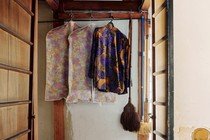 Clothes and brooms hang at the end of a corridor, above a red-patterned rug.