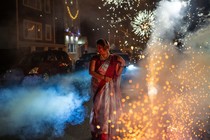 A woman stands amid fireworks in a street.
