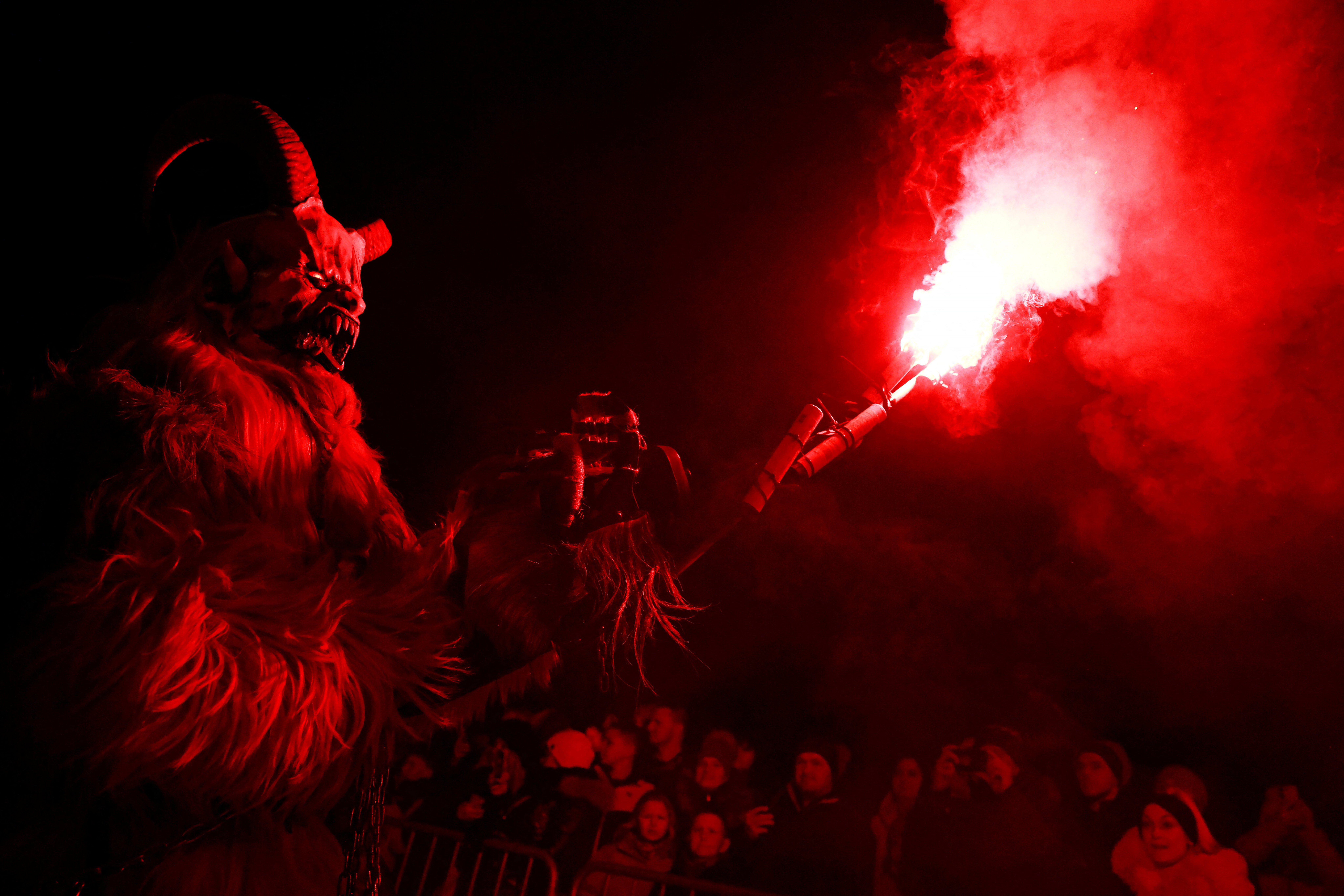 A person wearing a scary Krampus costume holds up a torch during a parade.