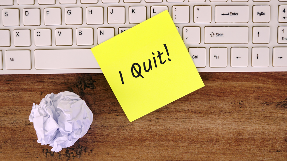 A post-it note with the words "I quit!" sits on top of a keyboard, next to a crumpled piece of paper.
