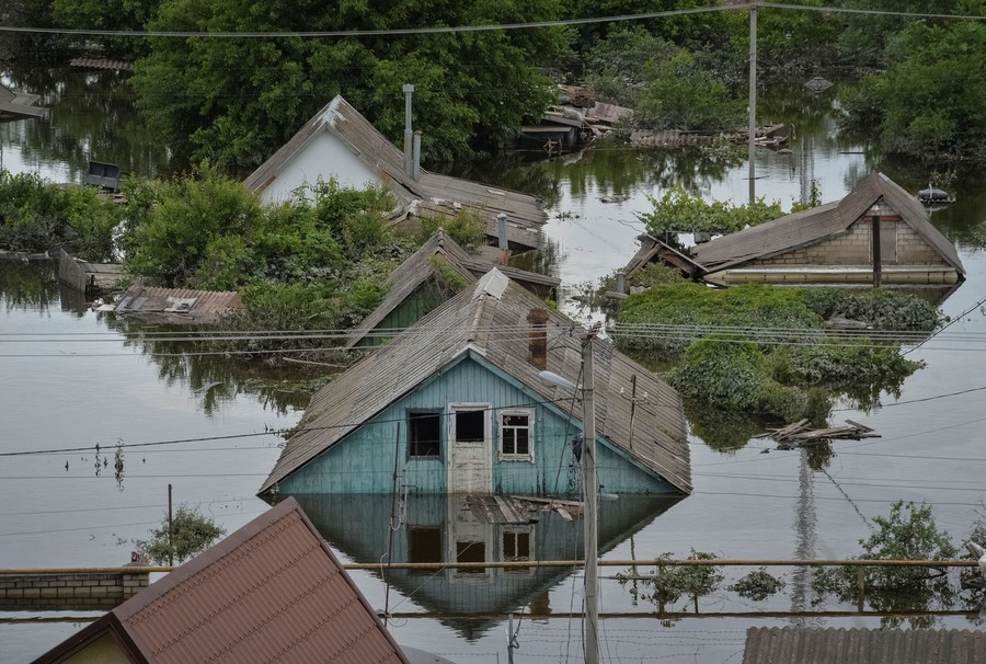 Several houses and trees, surrounded by floodwater