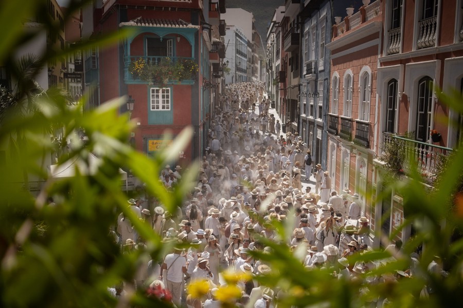 An elevated view of a crowd of people in a narrow city square, all wearing white clothing.
