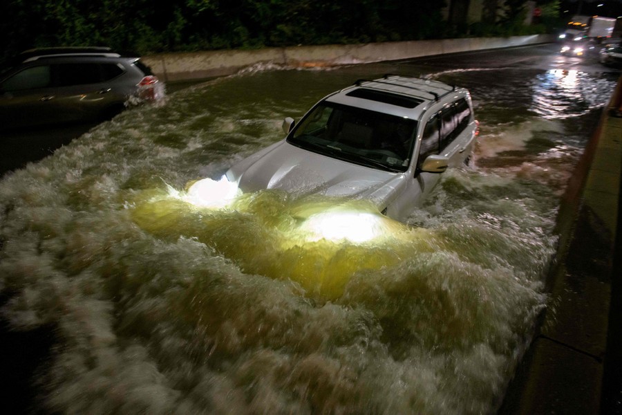 A car drives through deep water in a flooded road.