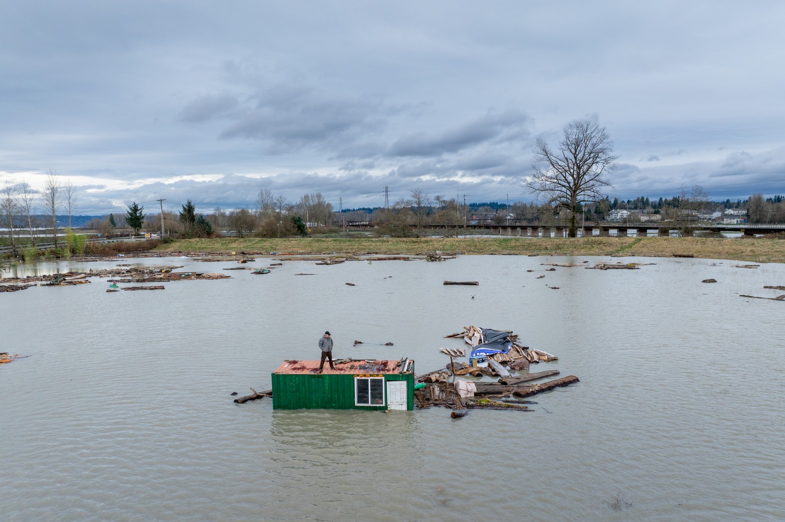 A person stands atop a small building engulfed by floodwater.