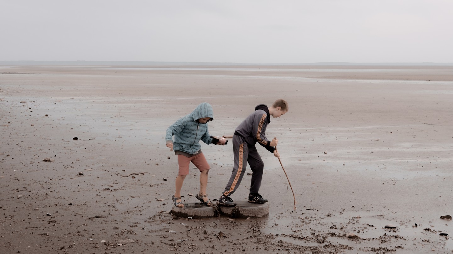 Two kids poke a stick into the mud of a dried reservoir.