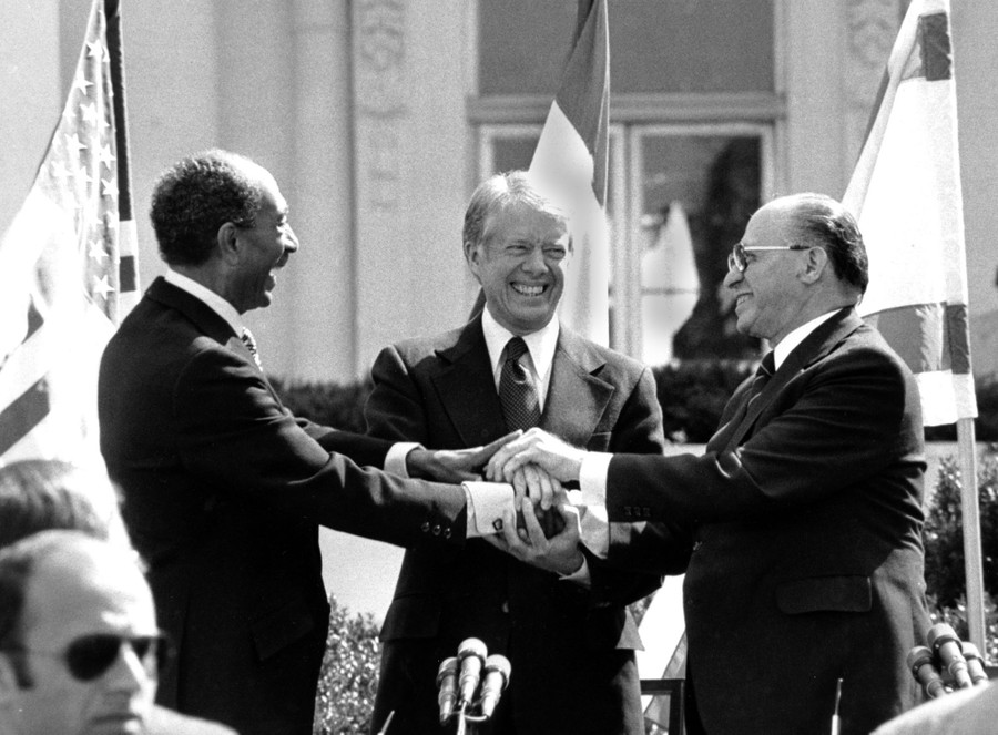 Jimmy Carter stands with Anwar Sadat and Menachem Begin, all shaking hands.