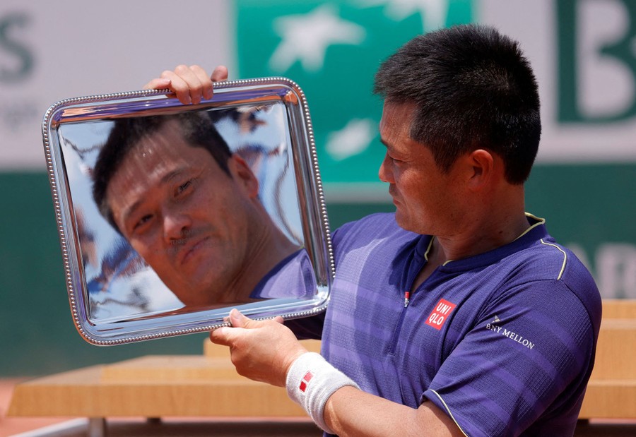 A tennis player's face is reflected in a silver platter trophy.