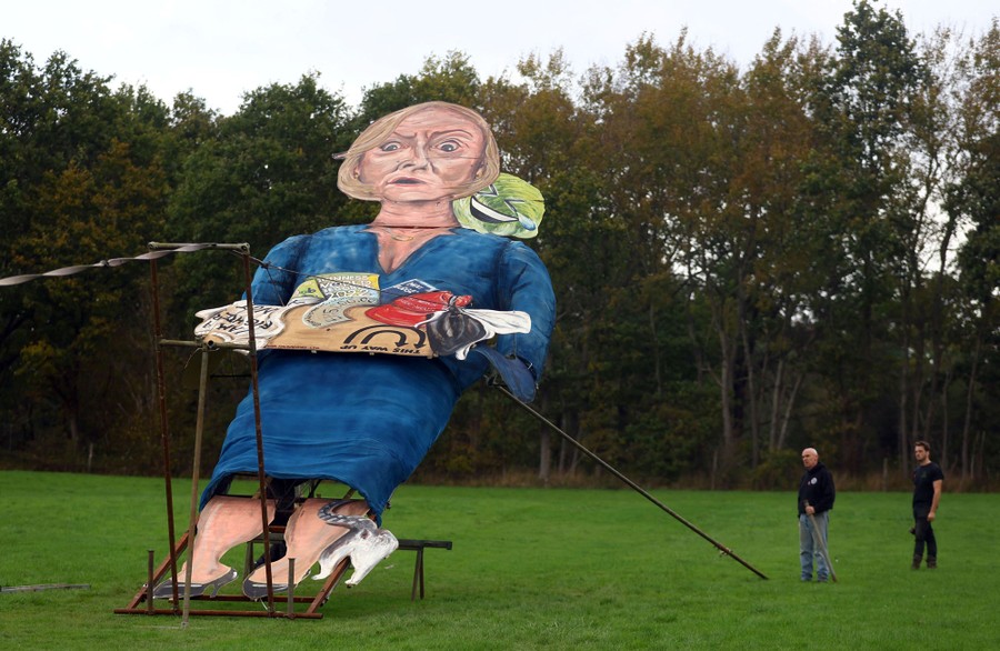 Njerëzit qëndrojnë pranë një statuje të gjatë të bërë që të duket si një karikaturë e ish-kryeministres britanike Liz Truss, ndërsa ajo është ngritur në vend.