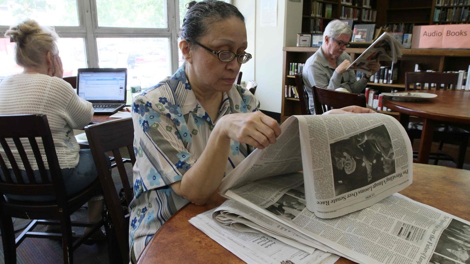 A woman reads a newspaper in a library.