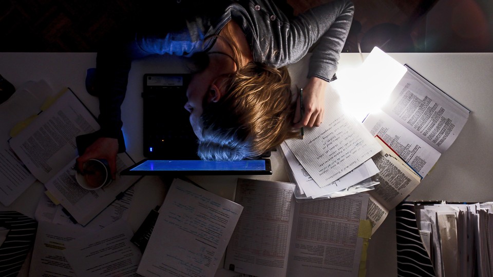 A woman sleeping on top of a laptop, surrounded by papers
