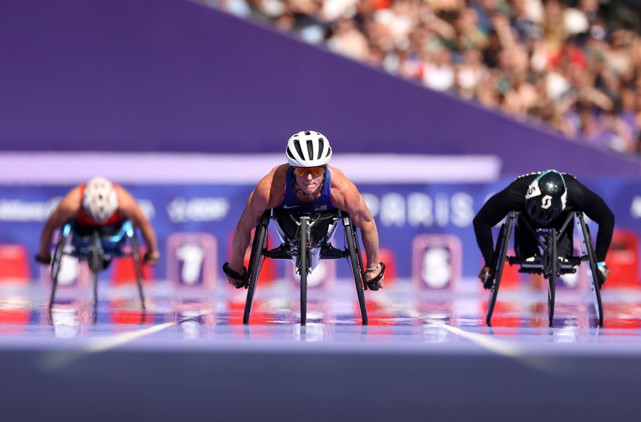 Several wheelchair racers are seen competing on a track.