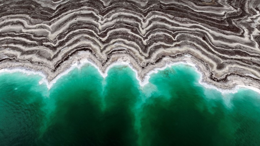 A drone's-eye view of green water and a striped, uneven shoreline