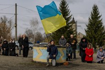 Ukrainians kneeling in a show of mourning, as one person holds a Ukrainian flag.