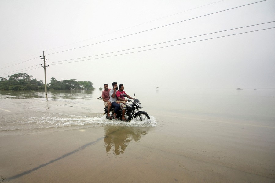 Three men ride a single motorcycle on a flooded road.