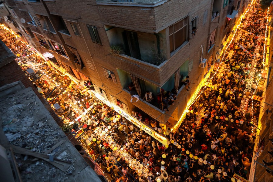 A view from a balcony of hundreds of people eating at long tables in a street below