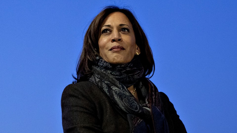 A photo of Kamala Harris wearing a black jacket and patterned scarf, against a blue backdrop