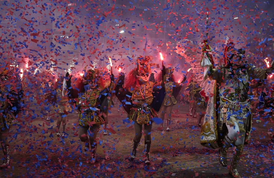People in traditional devil costumes walk in a parade surrounded by confetti falling from the sky.