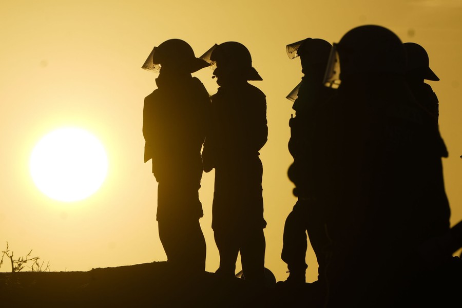 The sun rises behind several police officers wearing riot gear.