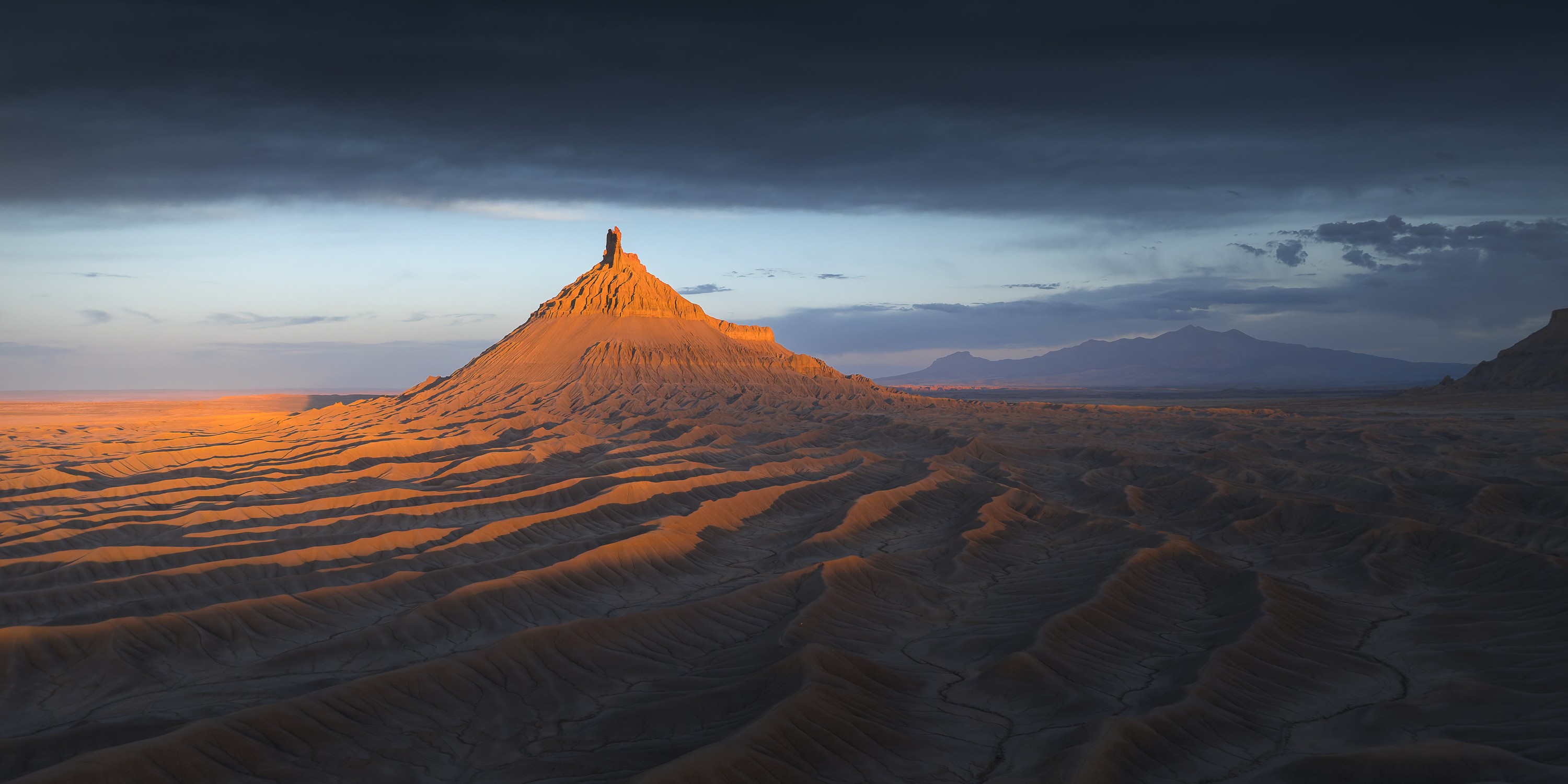 Sunset light over an iconic narrow butte, surrounded by a bare landscape of rippling ridges