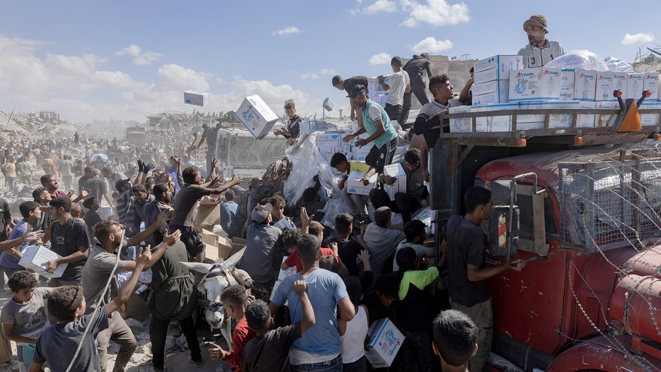 Color photograph of a crowd of Palestinians receiving aid from a convoy of trucks in Gaza