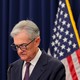 Jerome Powell looks down, with flags in the background