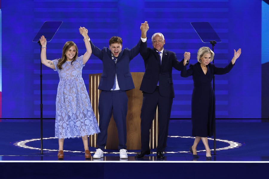 Democratic vice-presidential nominee Tim Walz stands onstage with his wife and two children, all holding their arms in the air.