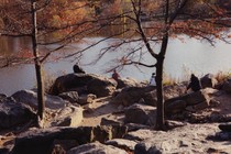 photo of people sitting on rocks next to water with fall foliage