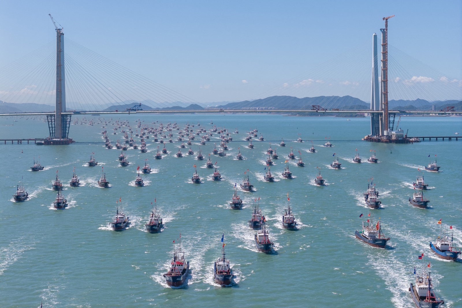 Dozens of fishing boats sail beneath a road bridge on their way out to sea.