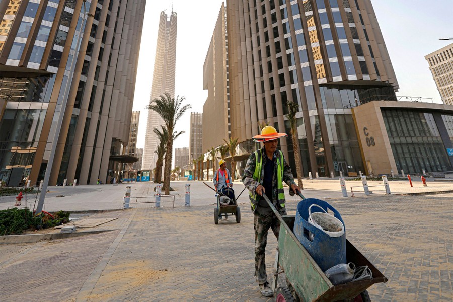 Two workers push carts among tall new buildings.