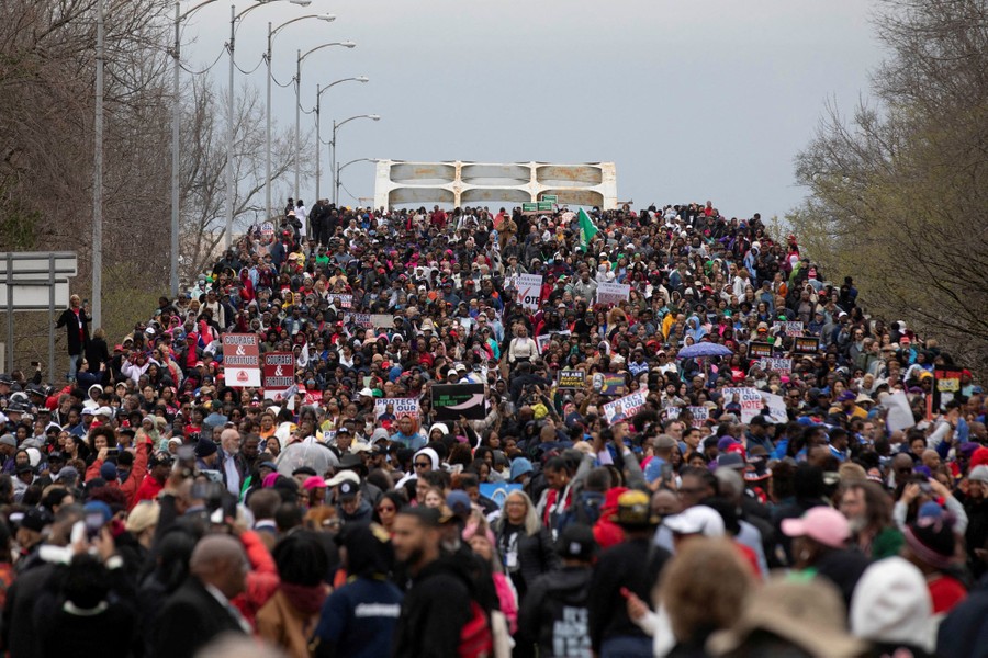 A large crowd marches across a road bridge, filling it.