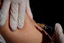 a gloved hand injecting a needle into an arm