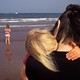 A woman holding a child and standing near another child, all by the ocean